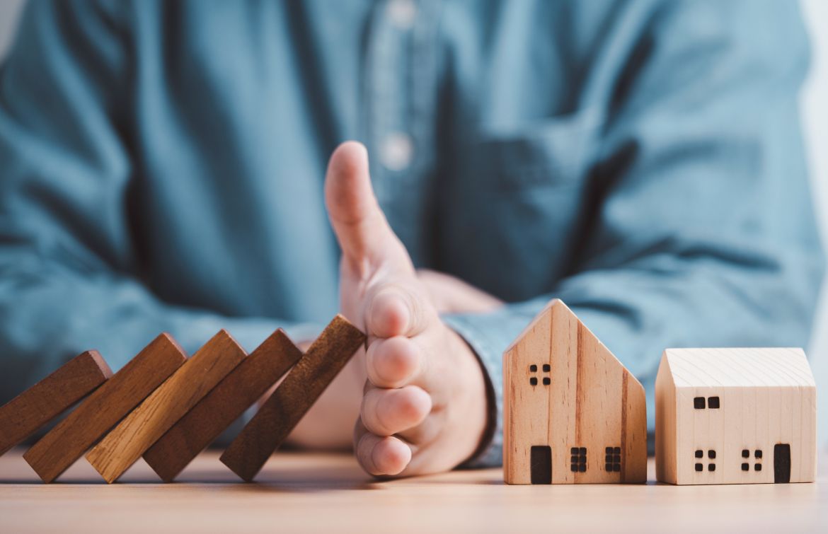 Man's hand stopping wooden blocks from falling onto house / building