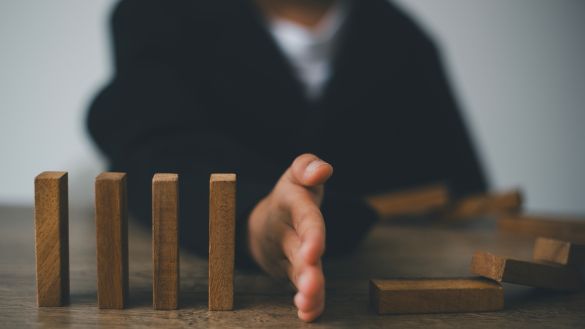 Businessman's hand preventing wooden blocks from falling on each other